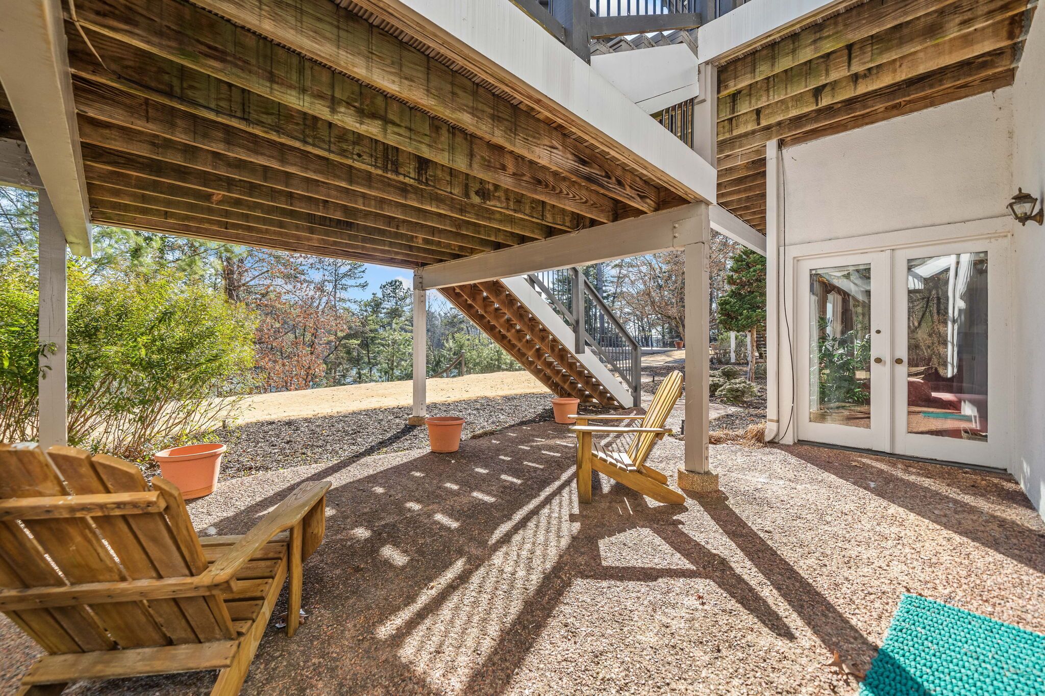 Un patio al aire libre con sillas de madera, una escalera y una puerta que da a una zona cubierta.