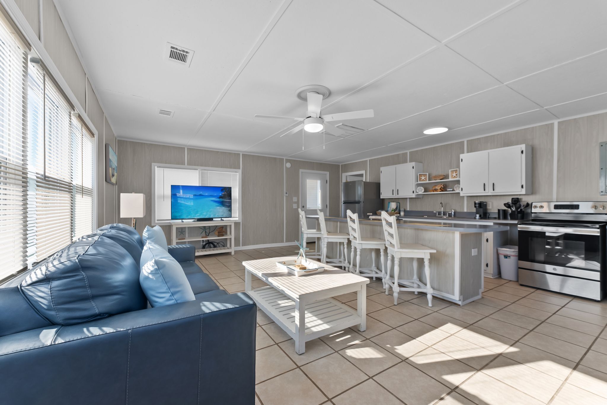 A modern kitchen with white cabinets, a central island, and a dining area with white chairs.