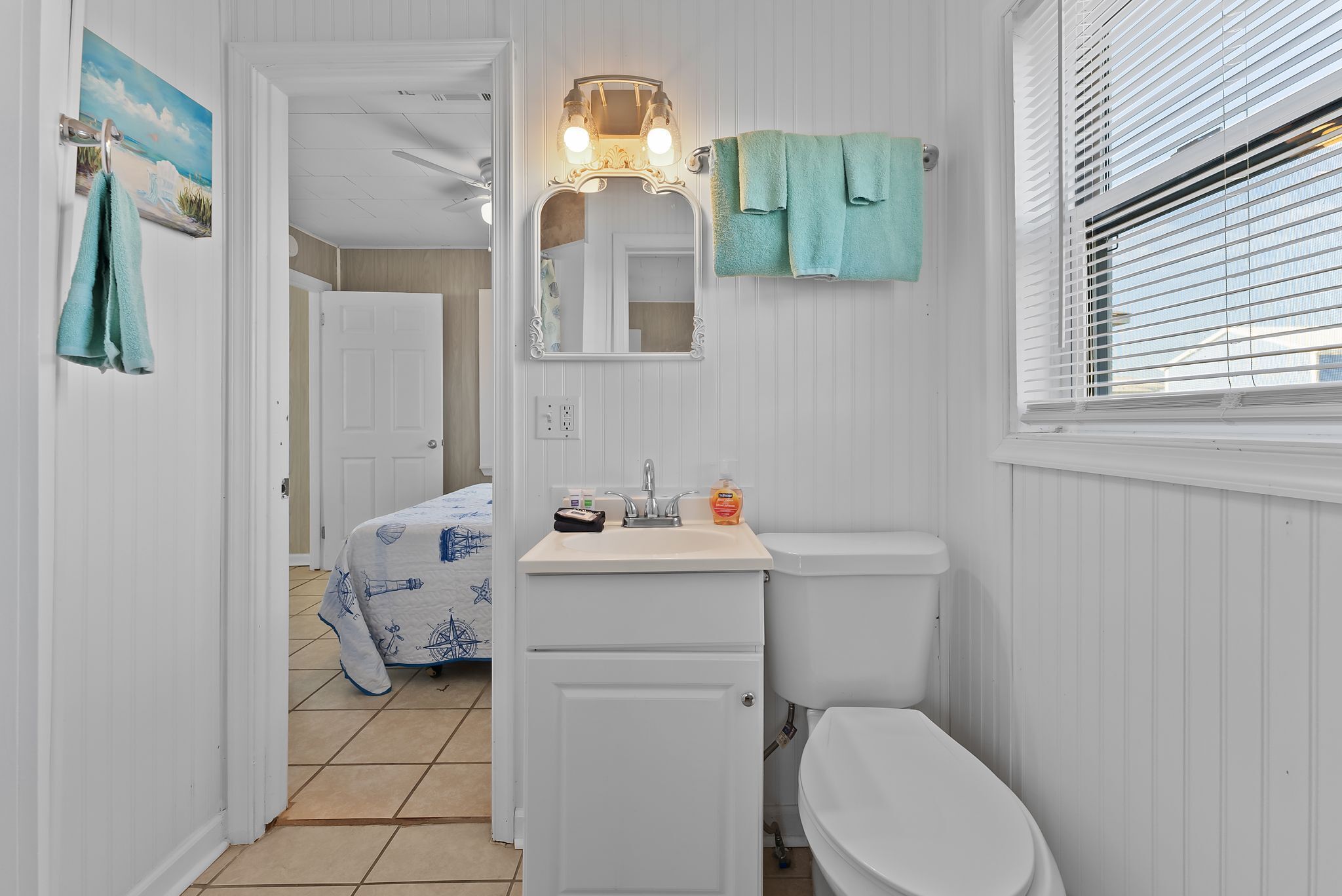 A bathroom with a toilet, sink, mirror, and window with blinds.