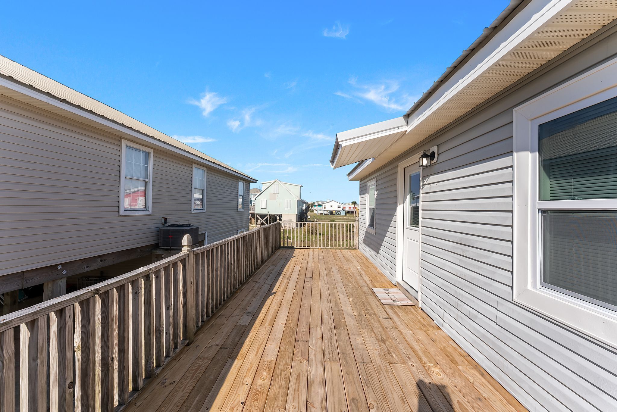 A narrow wooden deck connecting two single-story buildings with white siding and a metal roof.