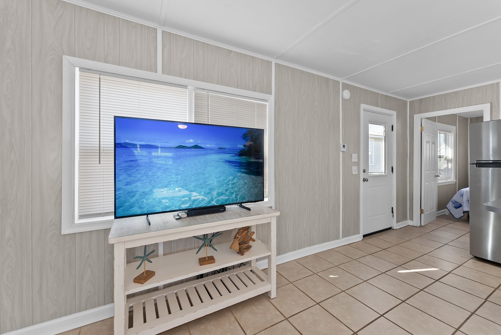 Una habitación con una televisión sobre un mueble blanco, una puerta y un refrigerador.
