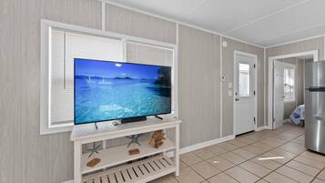 Una habitación con una televisión sobre un mueble blanco, una puerta y un refrigerador.