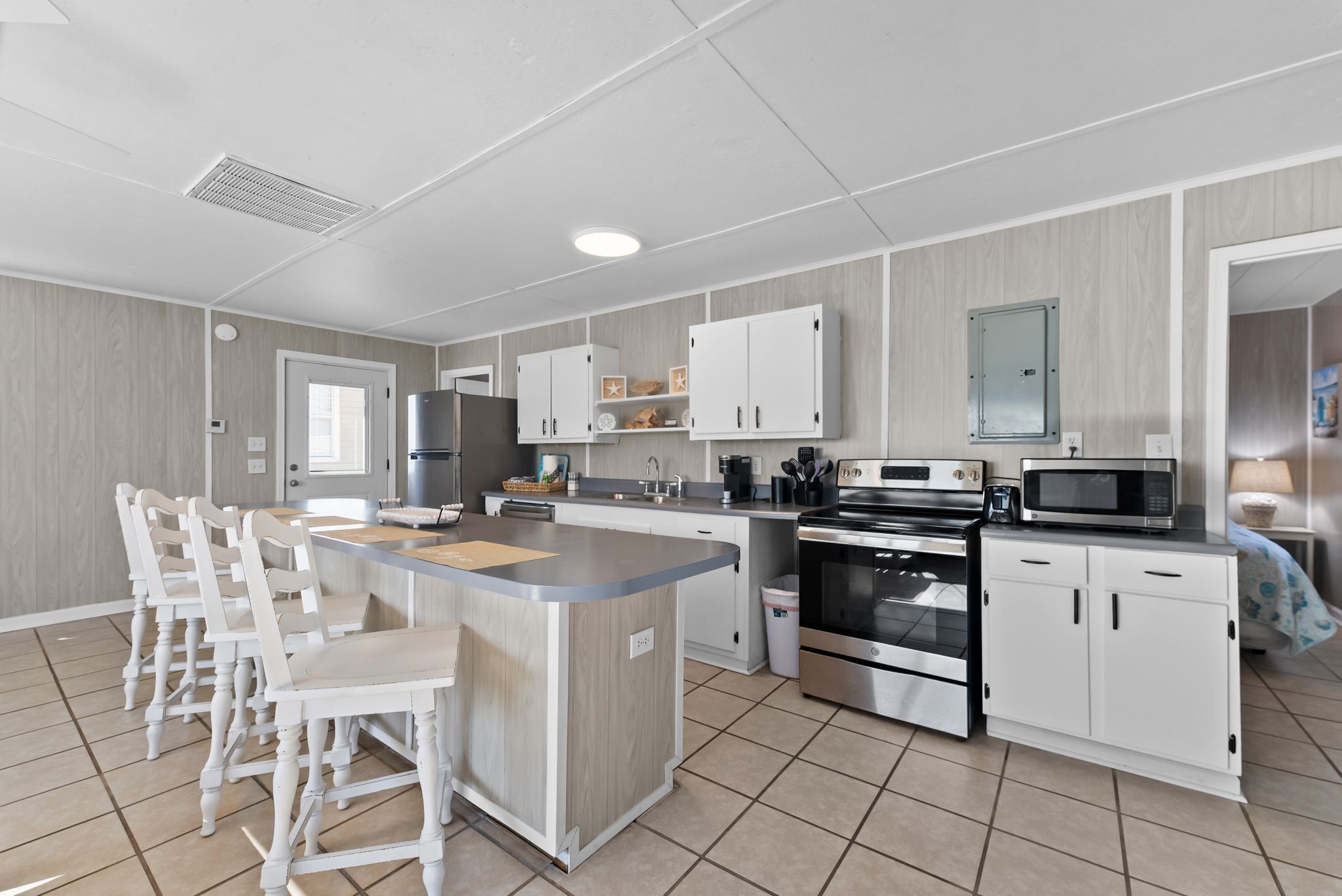 A modern kitchen with a central island, white cabinetry, stainless steel appliances, and a tiled floor.