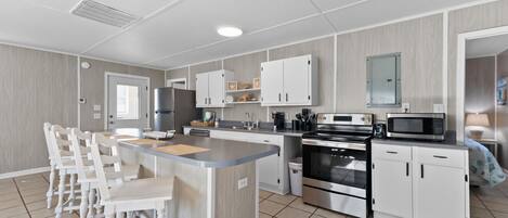 A modern kitchen with a central island, white cabinetry, stainless steel appliances, and a tiled floor.