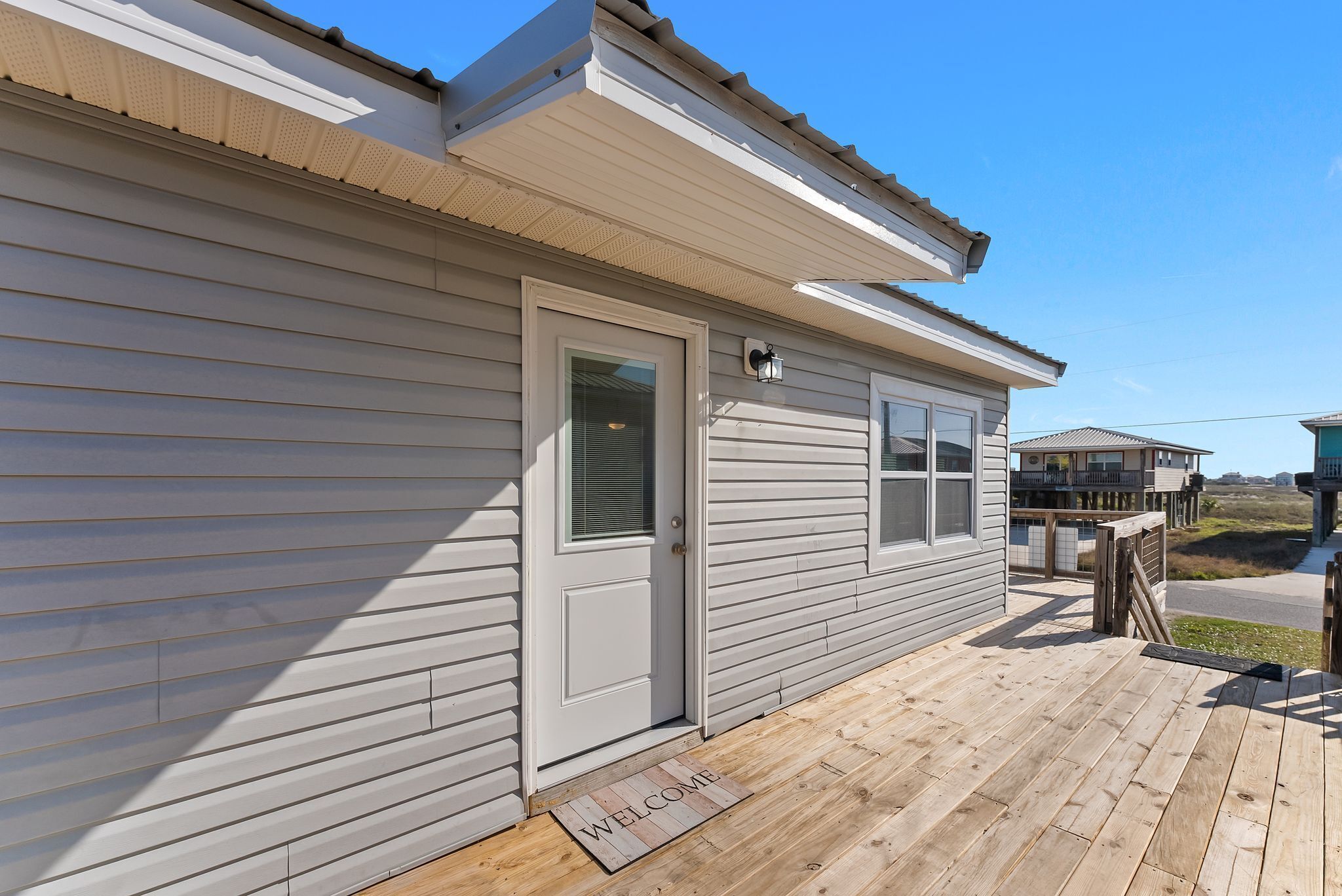 A house with a wooden deck, a white door, and a 'WELCOME' mat.