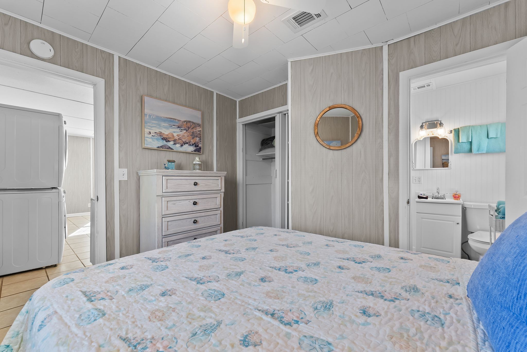Un dormitorio con cama, cómoda, armario y baño con espejo y lavamanos.