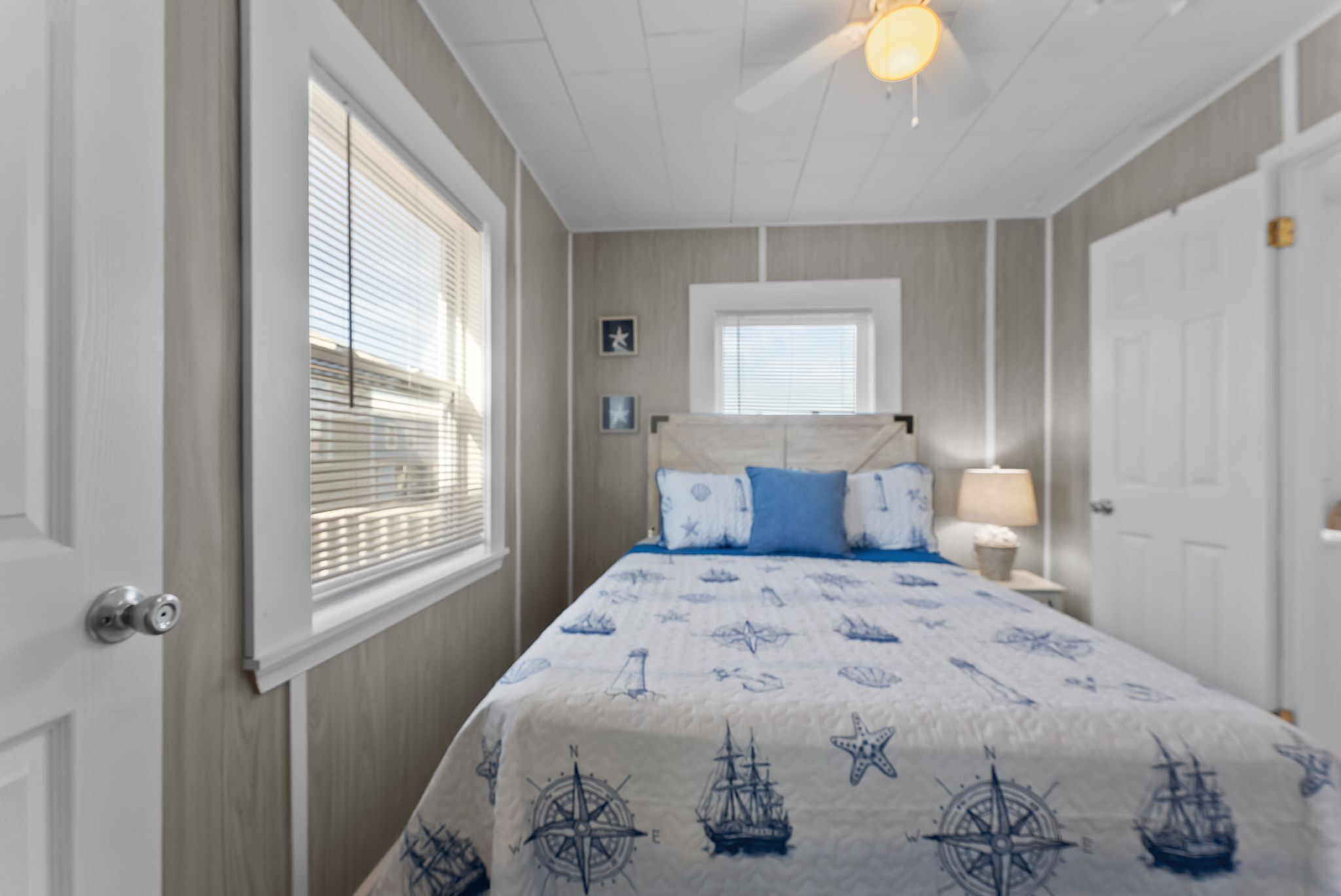 A bedroom with a bed, a nightstand, a lamp, a window with blinds, and a ceiling fan.