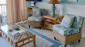 Un soggiorno con ventilatore a soffitto, televisore a schermo piatto, mobili in vimini e un tappeto blu.