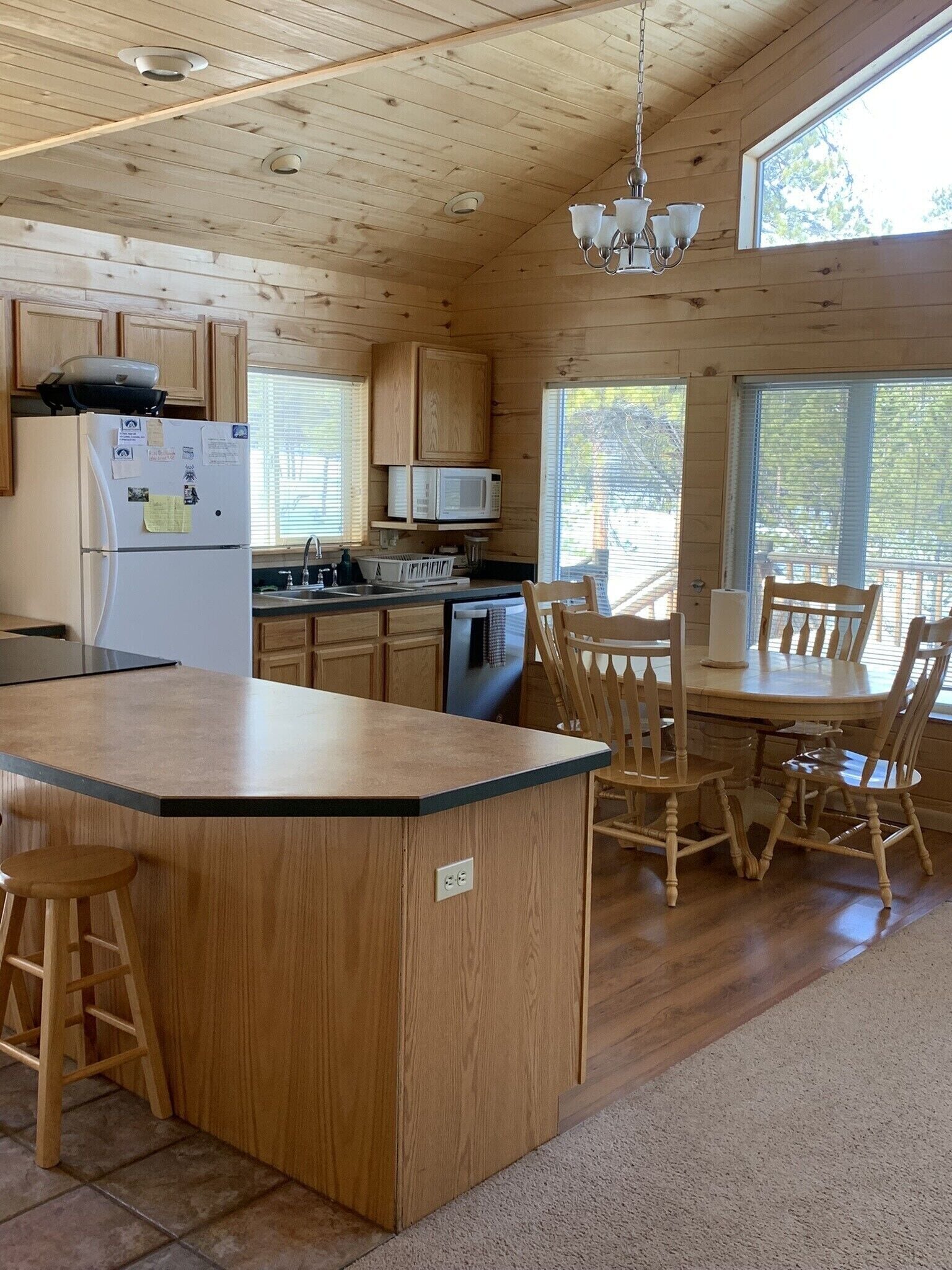 A wooden cabin interior with a kitchen, dining area, and a large window.