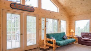 L’intérieur d’une cabane en rondins, avec un canapé vert, un fauteuil en cuir marron et un panneau indiquant « Billets pour le télésiège ».