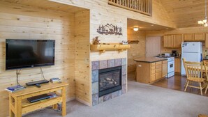 L'intérieur d'un chalet en bois comprend une télévision, une cheminée, une cuisine et un coin repas.