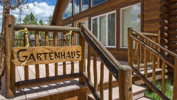 Une pancarte en bois portant l’inscription « Gartenhaus » est fixée à un escalier en bois menant à une cabane en rondins dotée de grandes fenêtres.