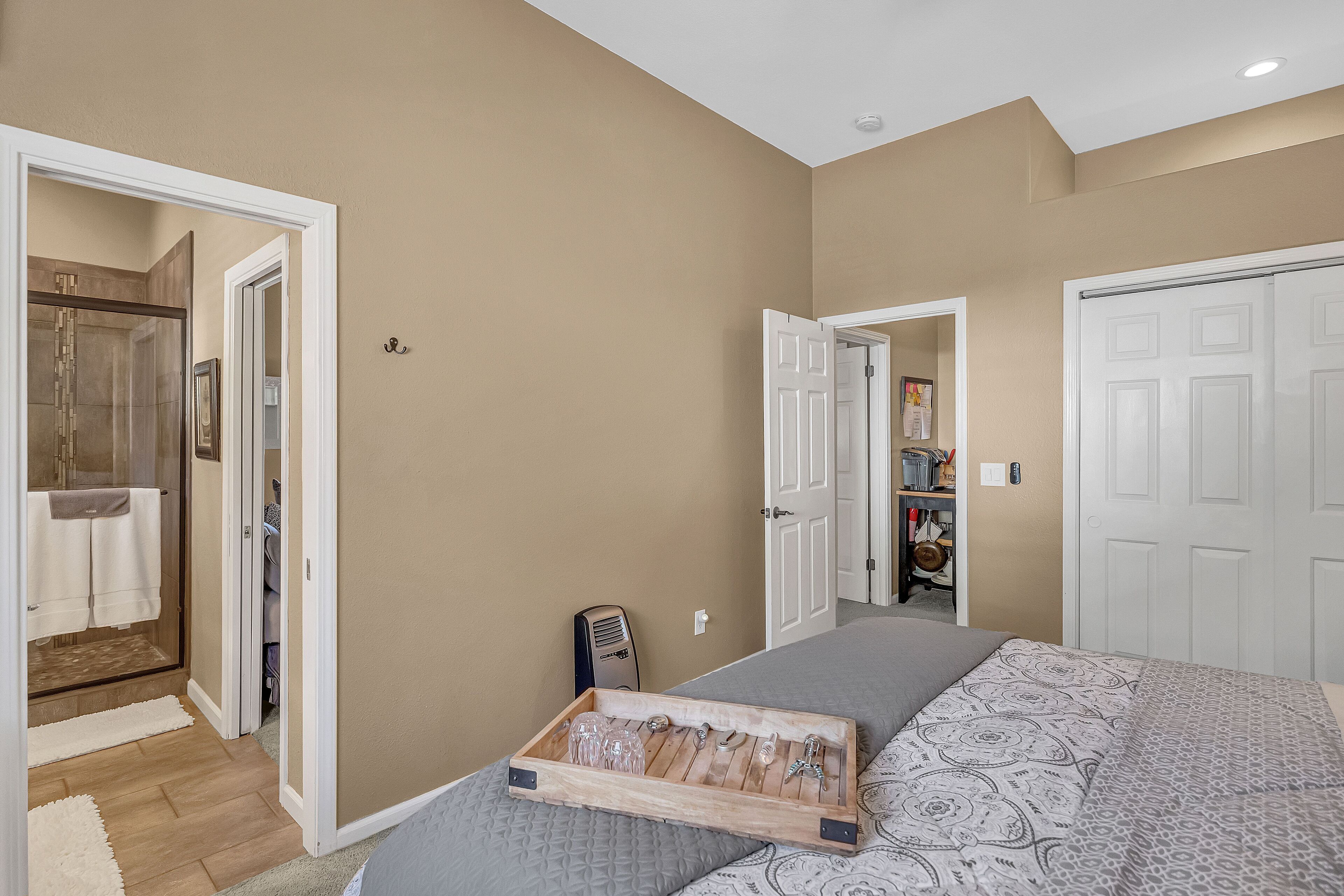 A bedroom with a bed, a wooden tray with glasses, a closet, and a bathroom with a shower.