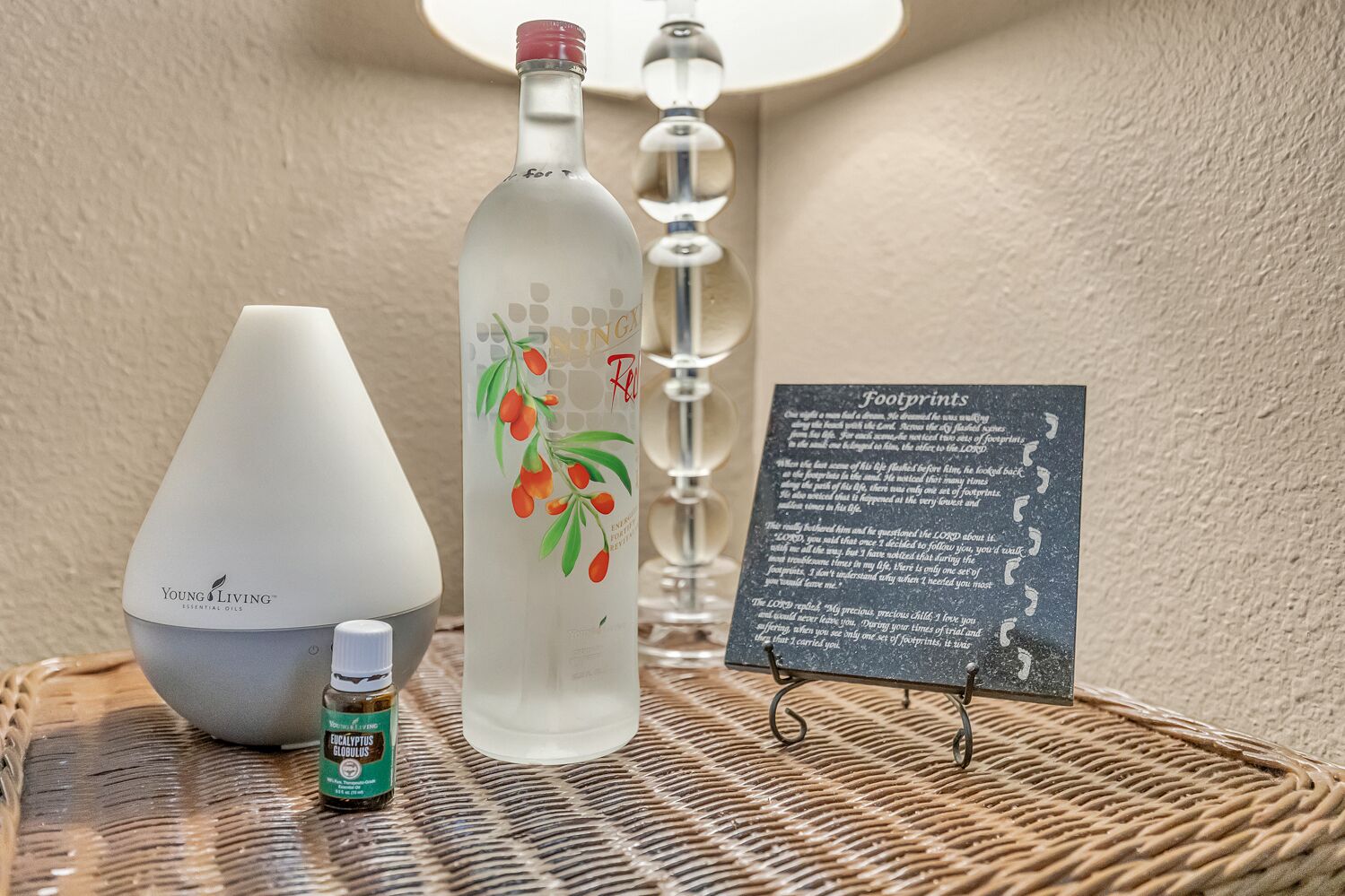 Une bouteille d’huiles essentielles Young Living, une bouteille en verre avec un bouchon rouge, un diffuseur blanc, un petit flacon d’huile essentielle d’eucalyptus et un panneau portant le titre « Empreintes ».