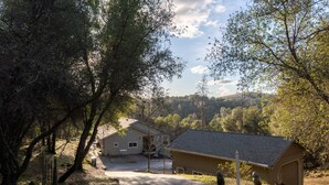 Zona residencial amb una casa i un garatge, envoltada d'arbres i un paisatge amb turons.