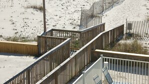 Pasarela de madera que conduce a una zona de playa arenosa con valla de madera y barandilla metálica.