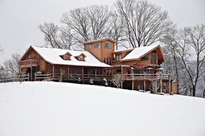 Eine große Holzhütte mit mehreren Stockwerken und einem mit Schnee bedeckten Dach, umgeben von Bäumen.
