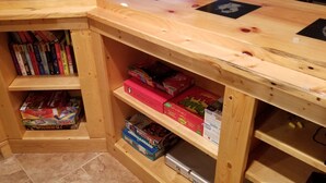 A corner of a room with wooden shelving units containing books and board games.