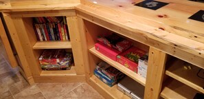 Una esquina de una habitación con estanterías de madera que contienen libros y juegos de mesa.