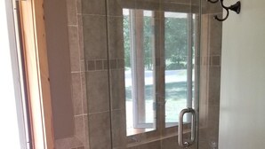 A shower room with a glass door, a white rug, and a window.
