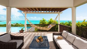 A covered outdoor seating area with wicker furniture, a hammock, and a view of the ocean.