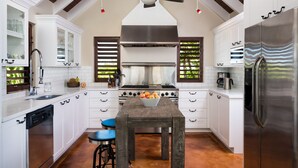 A modern kitchen with white cabinetry, a central island, a stainless steel refrigerator, and a ceiling fan.