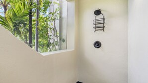 A corner of a room with a window overlooking greenery, a black floor, and a wall-mounted light fixture.
