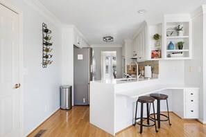 A modern kitchen with white cabinetry, a stainless steel refrigerator, and a built-in island with stools.