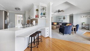 A modern kitchen with white cabinetry, a central island with stools, and a dining area with a dark blue sofa and wooden coffee table. - Lakefront, Swimming pool family home minutes from downtown Nashville (Hendersonville)