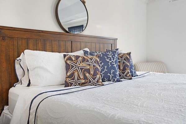 A neatly made bed with a wooden headboard, white bedding, and patterned pillows.