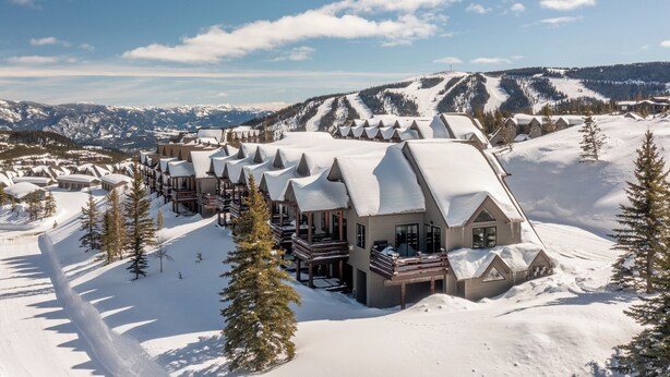Un albergue cubierto de nieve con varias cabañas, cada una con un balcón, frente a un paisaje montañoso.