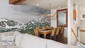 Una sala de estar acogedora con un sofá grande, una mesa de comedor con sillas y un mural de montañas en la pared.