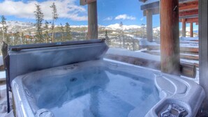Un jacuzzi con vistas a montañas y árboles nevados.