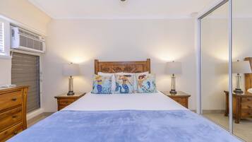 Un dormitorio con una cama, dos mesitas de noche con lámparas, un aparador de madera y un espejo grande.