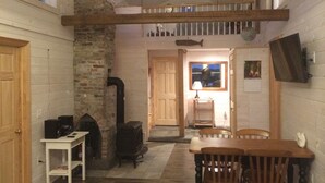 A cozy room with a fireplace, wooden furniture, a loft area with a balcony, and a wall-mounted TV. - Beautifully Renovated Ocean Front Cottage With Spectacular Views.. (Jonesport)