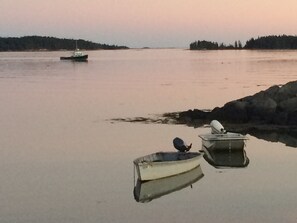 Una superficie d'acqua tranquilla con due piccole imbarcazioni ormeggiate vicino a una riva rocciosa.