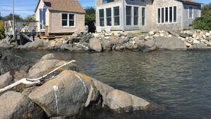 A waterfront property with a large house and a smaller cabin, both featuring multiple windows and a stone foundation. - Beautifully Renovated Ocean Front Cottage With Spectacular Views.. (Jonesport)