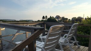 A wooden deck with two white plastic chairs facing a body of water. - Beautifully Renovated Ocean Front Cottage With Spectacular Views.. (Jonesport)