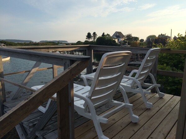 A wooden deck with two white plastic chairs facing a body of water. - Beautifully Renovated Ocean Front Cottage With Spectacular Views.. (Jonesport)