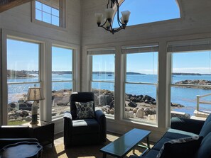 A sunlit room with large windows overlooking a rocky shoreline and calm water. - Beautifully Renovated Ocean Front Cottage With Spectacular Views.. (Jonesport)