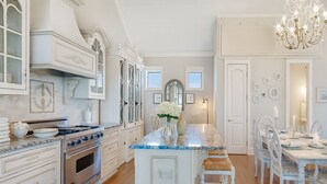 Een ruime keuken met witte kasten, een marmeren aanrechtblad en een eethoek met witte stoelen en een tafel.
