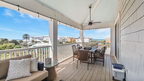 Een overdekt balkon buiten met een tafel, stoelen, een bank en een plafondventilator.