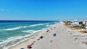 Een strand met rijen strandparasols en ligbedden, een zandstrand en gebouwen op de achtergrond.