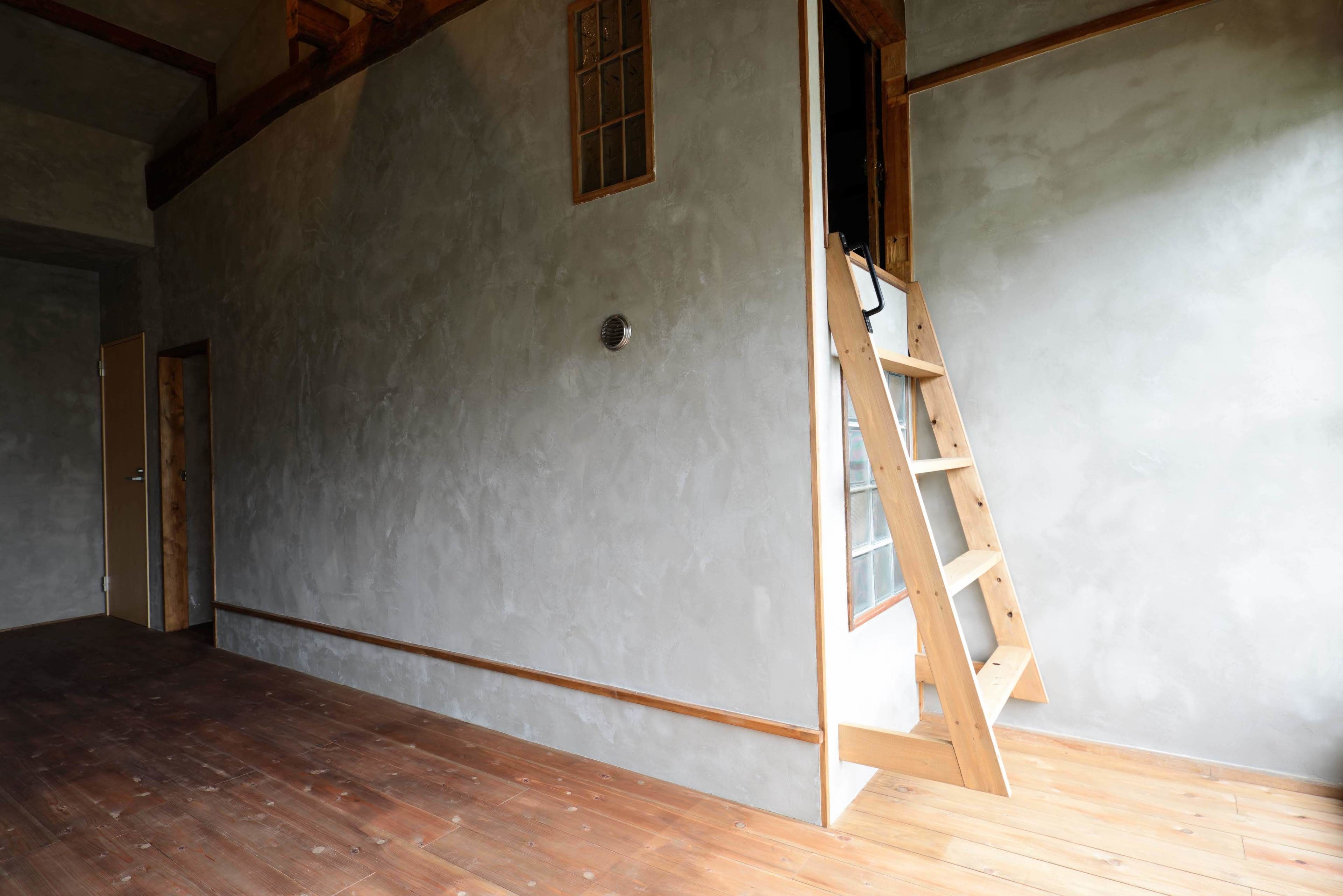 A room with a wooden floor, a ladder leaning against the wall, and a door leading to another room.