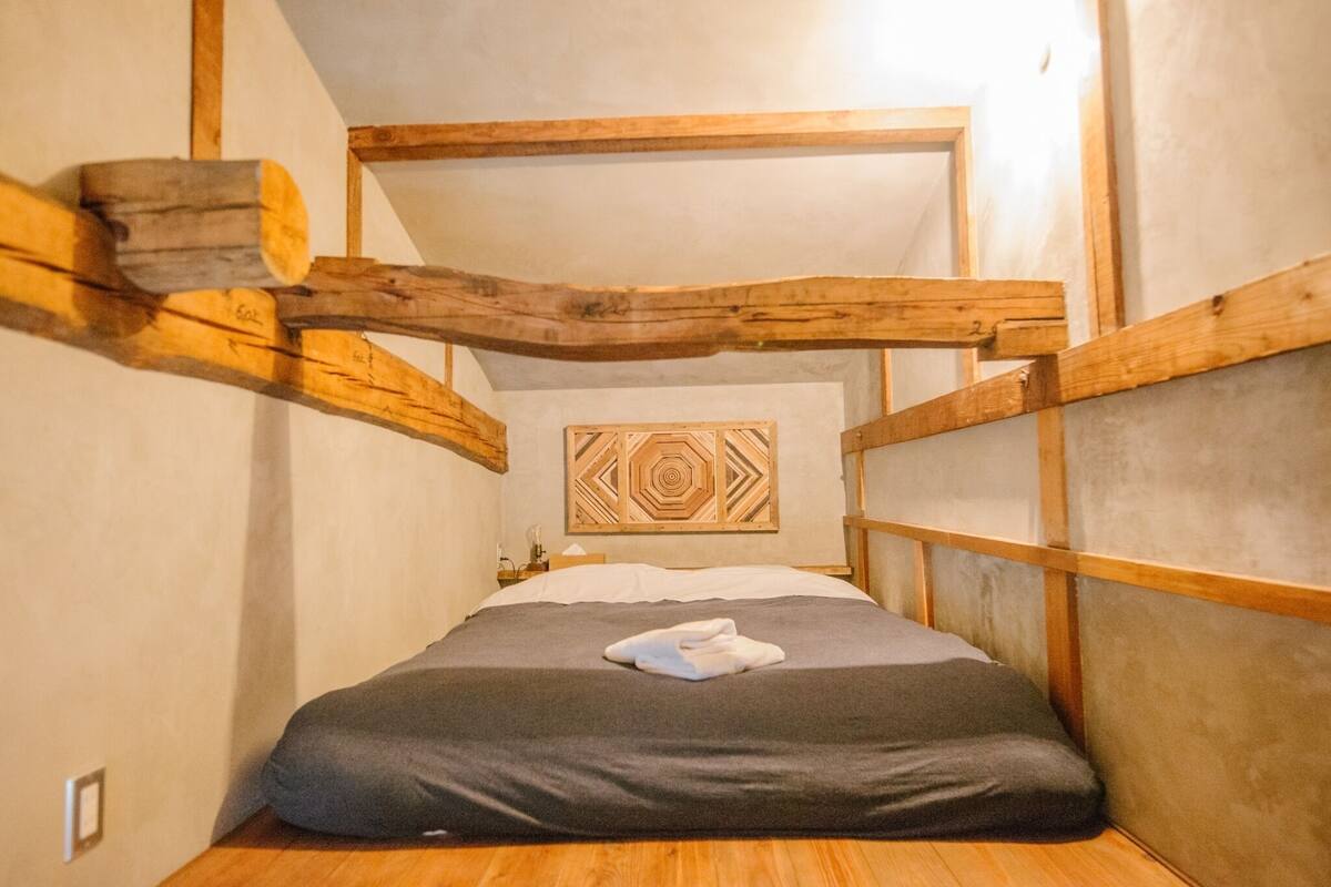 A bunk bed with a wooden headboard, a geometric wall art piece, and a small bedside table with a lamp.