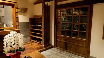 Un interior japonés tradicional con una puerta de madera, un zapatero y un jarrón con flores blancas.