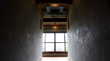 A narrow hallway with a large window at the end, wooden beams on the ceiling, and a visible air conditioning unit.