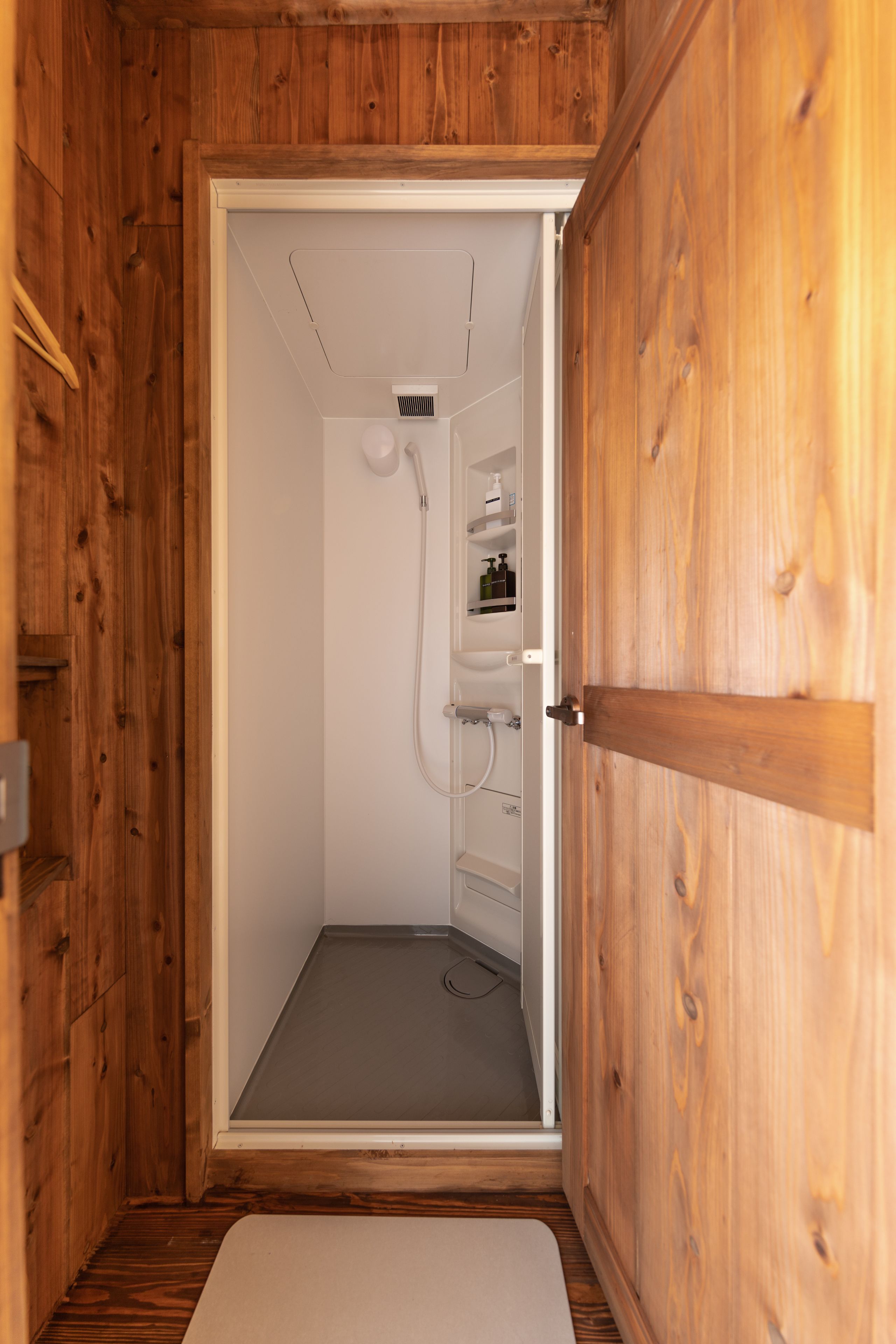 A wooden-paneled bathroom with a shower, a toilet, and a sink.