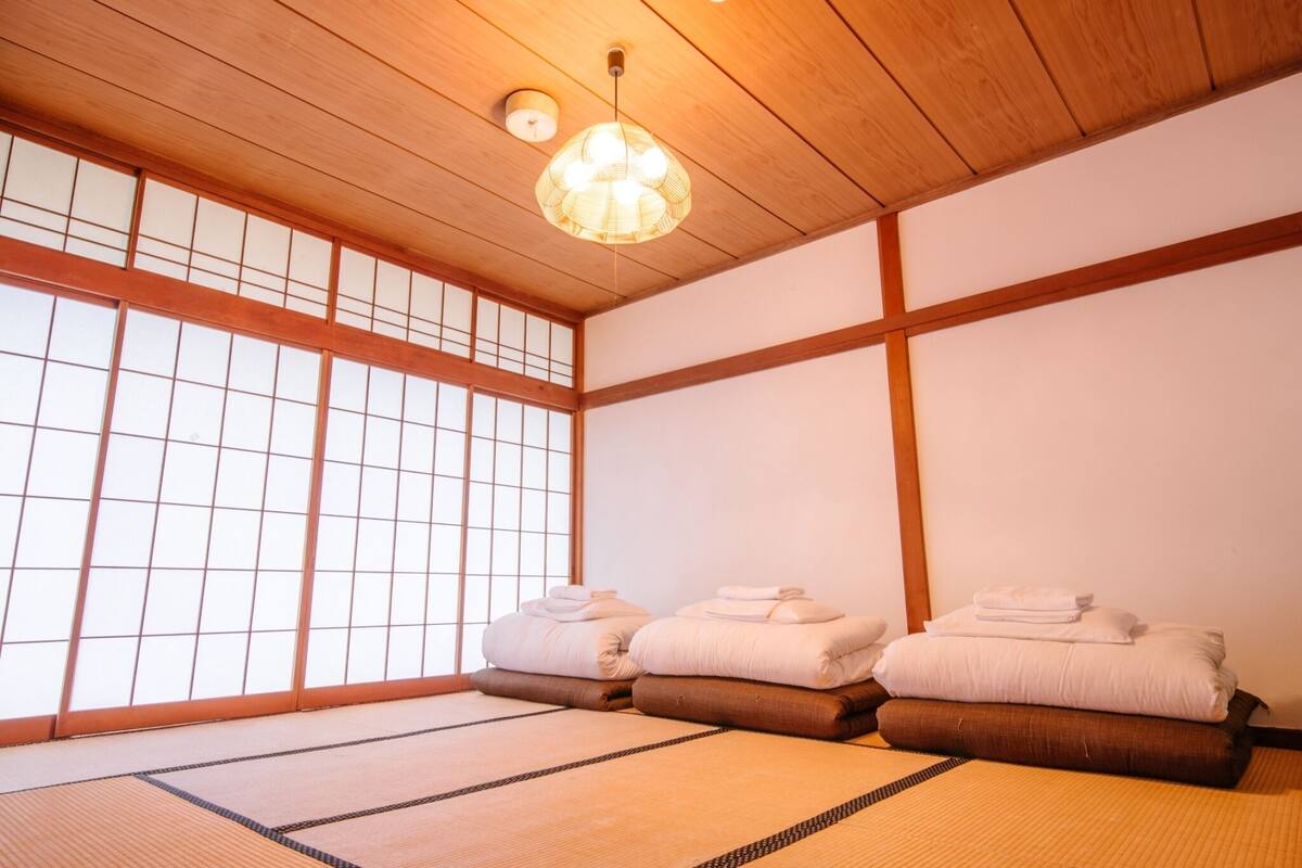 A traditional Japanese room with tatami flooring, a shoji screen, and a hanging light fixture.
