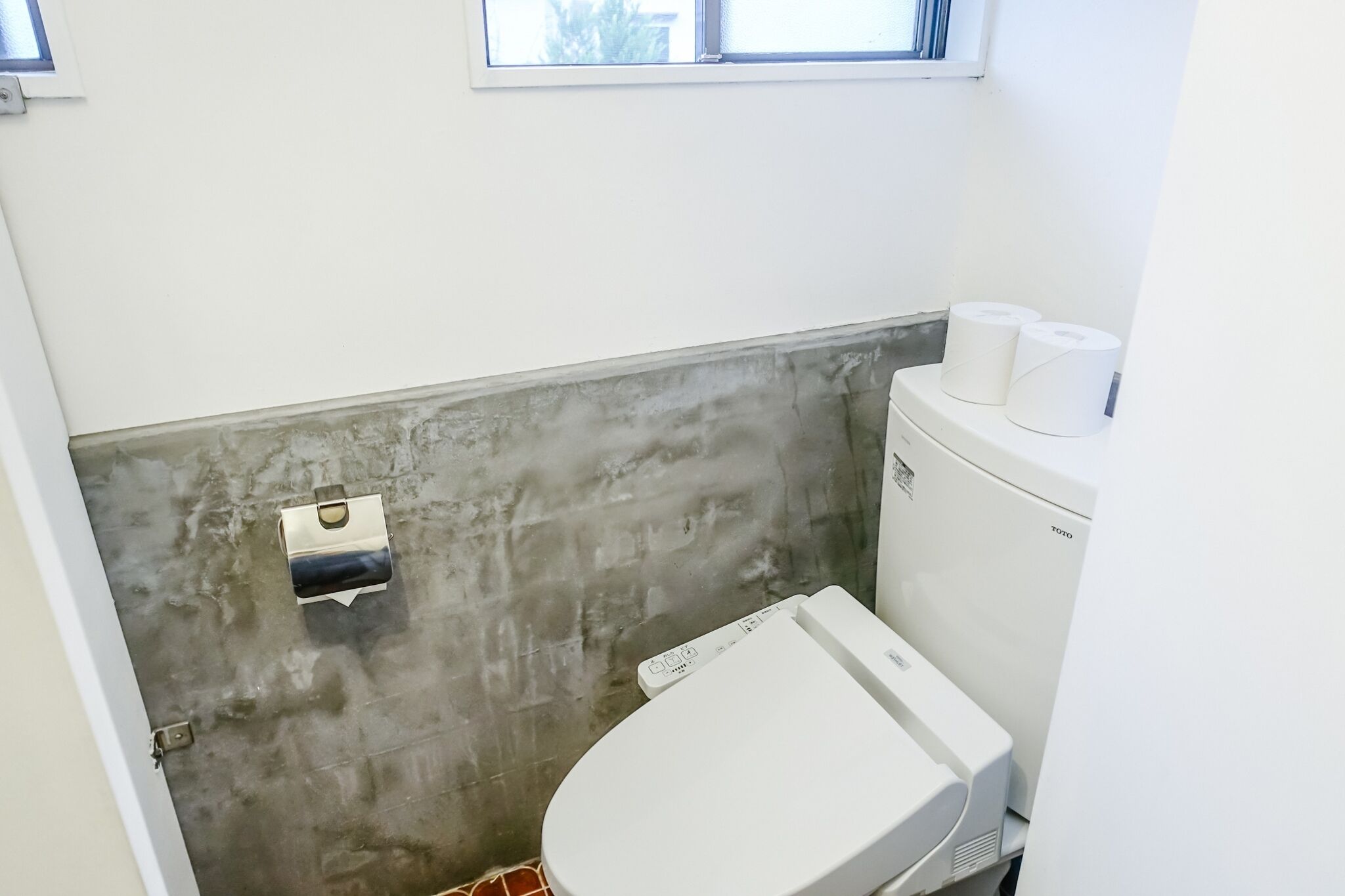 A small bathroom with a toilet, a trash bin, and a toilet paper holder.